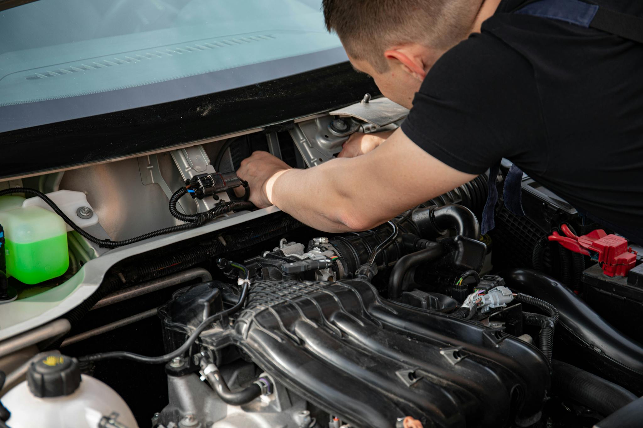 Mechanic fixing a car engine under the hood showing detailed components.